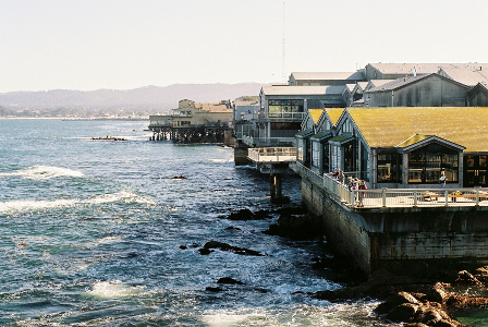 [White-capped water amid rocks on the ground. The buildings in the bay are up on piers or stilts.]